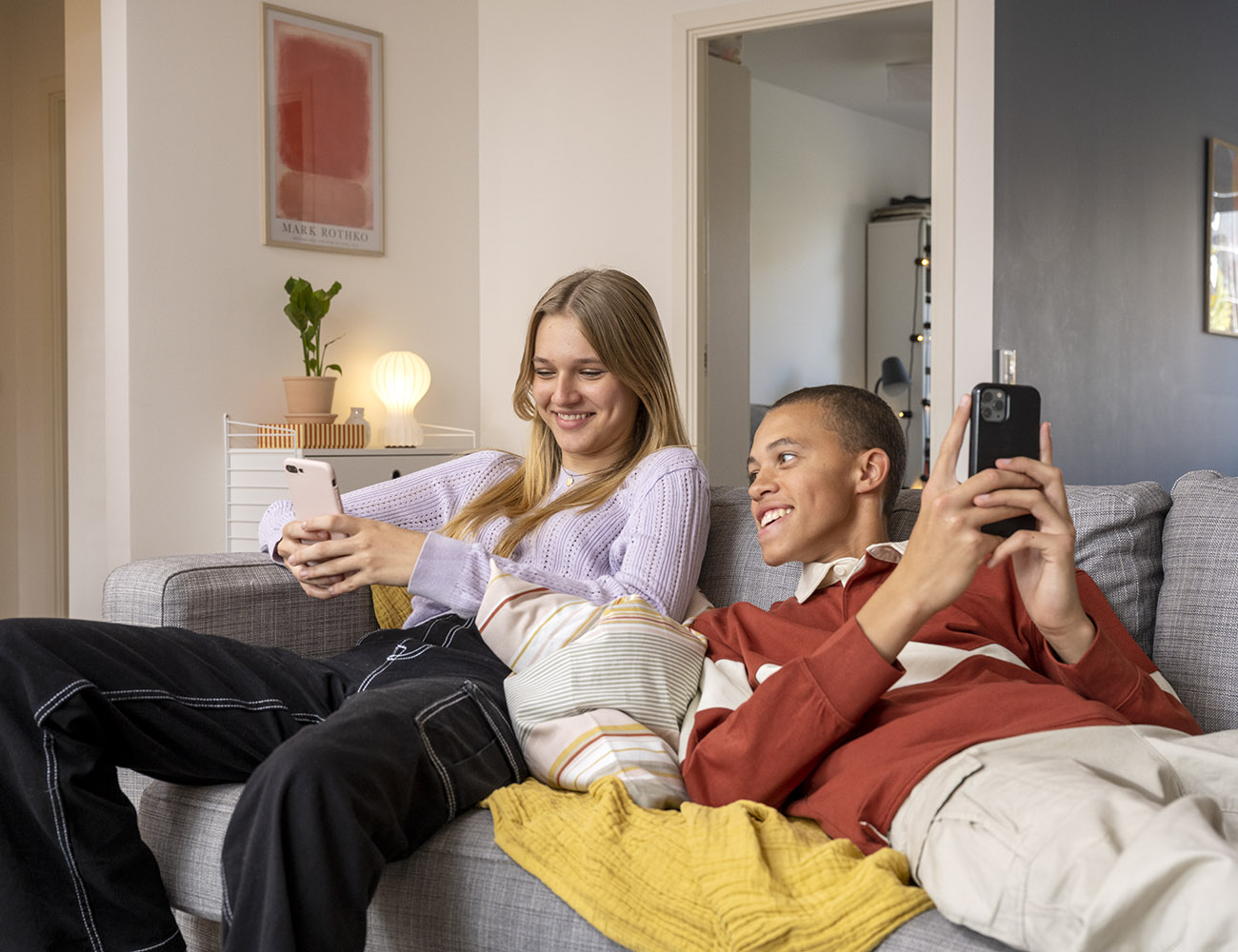 En tjej och en kille sitter i en soffa med varsin mobiltelefon i handen