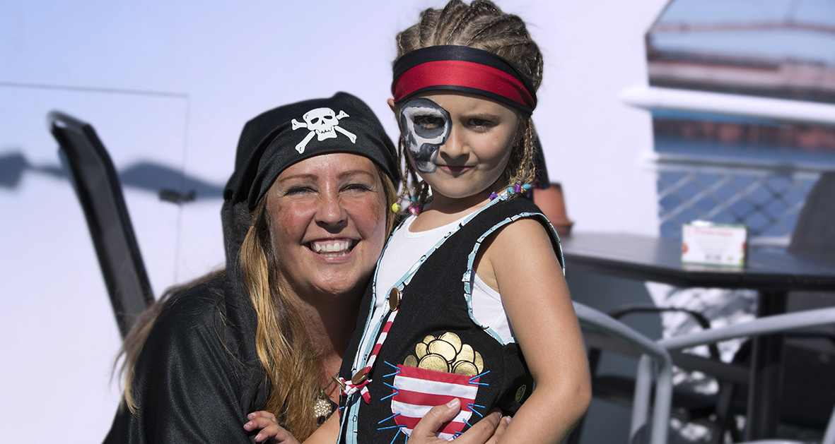 En kvinna i pirathat och en liten tjej med piratkläder står och ler in i kameran