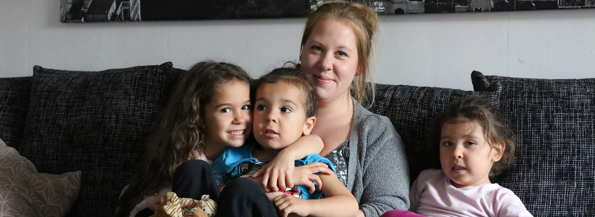 En mamma och tre barn sitter i en soffa