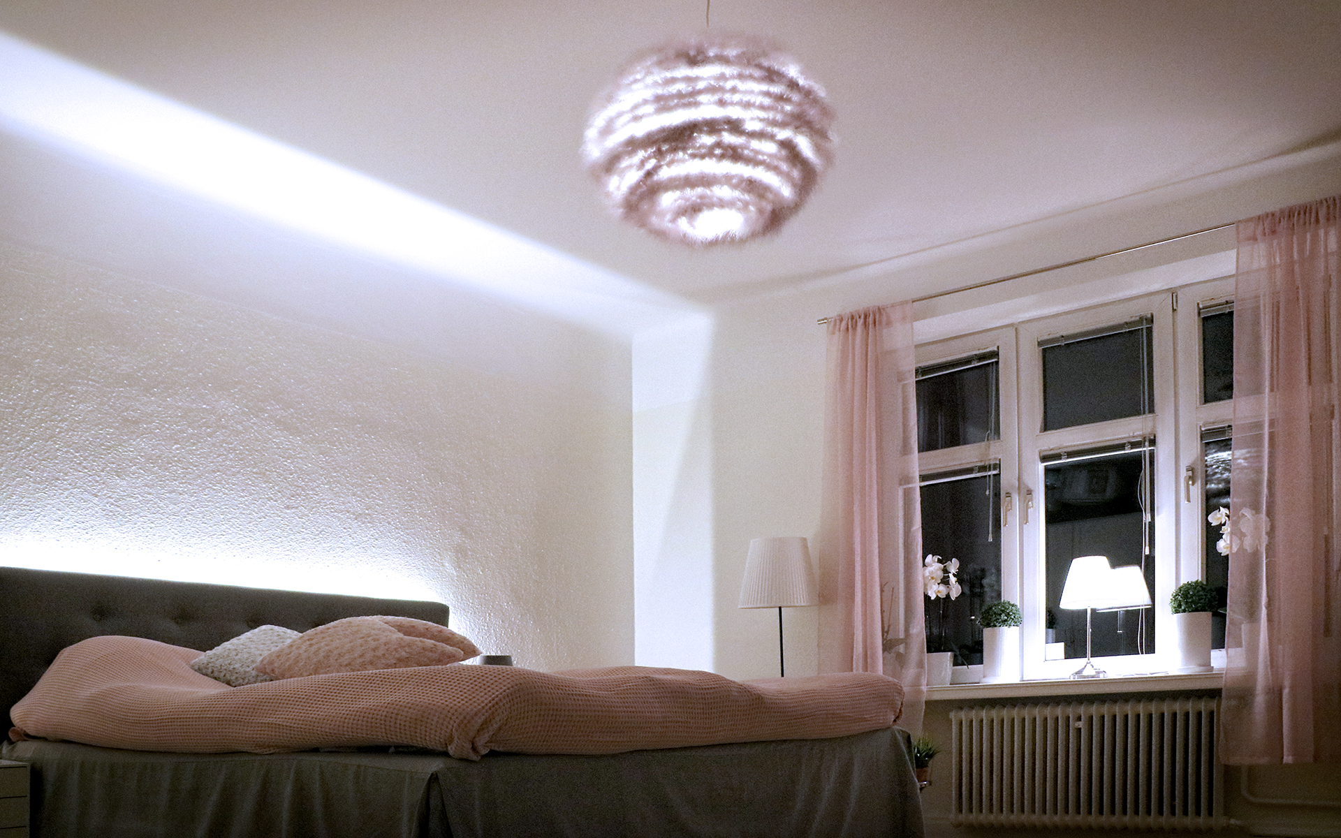 Ett vitt sovrum med en stor fluffig taklampa