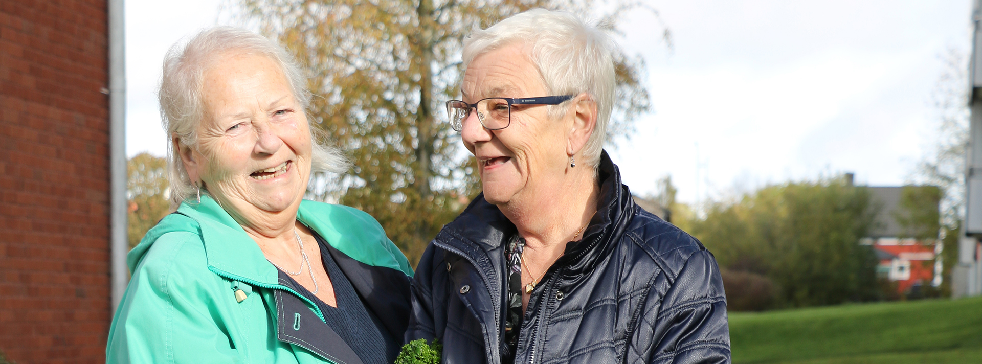 Två äldre kvinnor står ute på en gård och skrattar