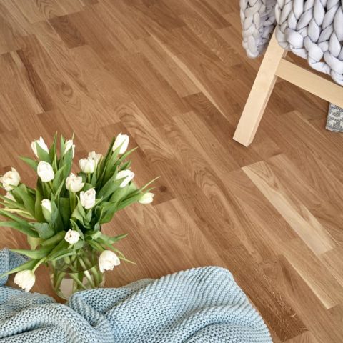 En närbild på ett parkettgolv där man ser en tulpanbukett och en fåtölj med en filt på