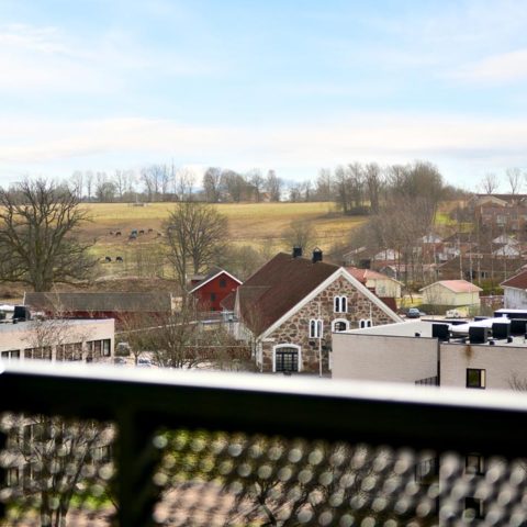 En närbild på ett balkongräcke där man ser några villor och grönområde