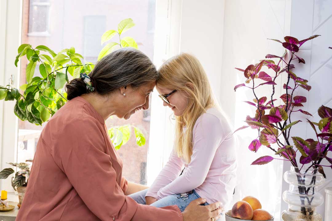 stående kvinna och sittande barn panna mot panna i en ljus boendemiljö