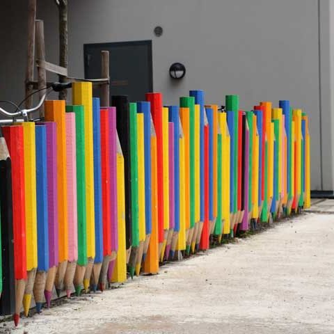 Ett staket som är formen av massa olika färgglada pennor där spetsen är neråt.