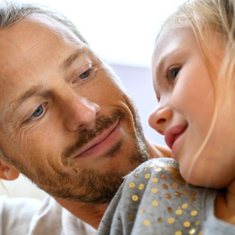 En man med skägg och en tjej med ljust hår och en tröja med palettdetaljer som sitter i en soffa.