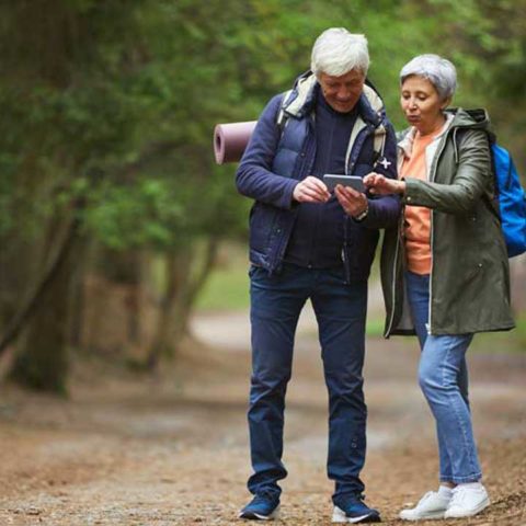 En man och en kvinna är i en skog och tittar båda på en karta i handen