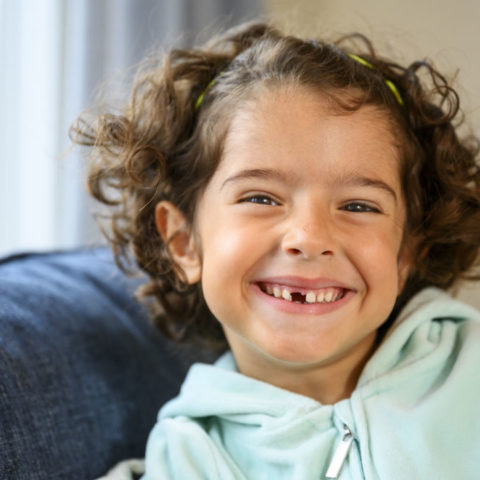 En liten ficka med en turkos hoodtröja ler mot kameran och har en glögg