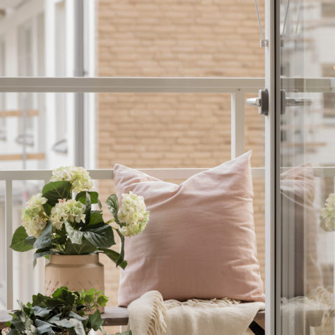 En balkong med en liten bänk som det står en blomma och en rosa kudde på