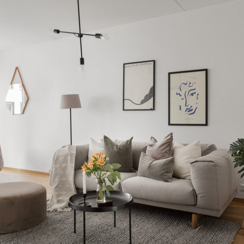 Ett ljust vardagsrum med en beige soffa och ett svart runt soffbord