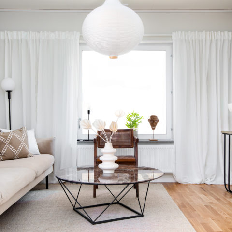 Ett ljust rum med en beige soffa och långa ljusa gardiner