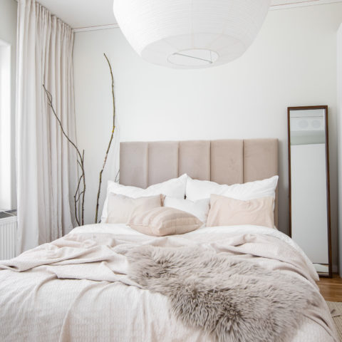 Ett vitt och ljust sovrum med en stor säng med massa ljusa textilier i