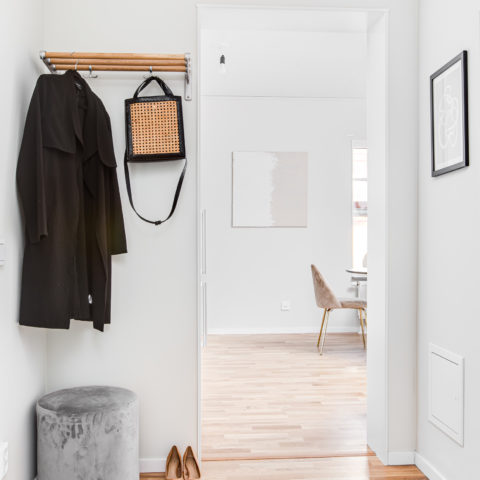 En vit hall med en hatthylla som det hänger en jacka och en väska på