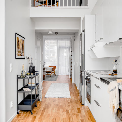 Vy från köket där man ser den vita köksmiljön till höger och en svart serveringsvagn till vänster. Ovan ser man en del av ett sovloft