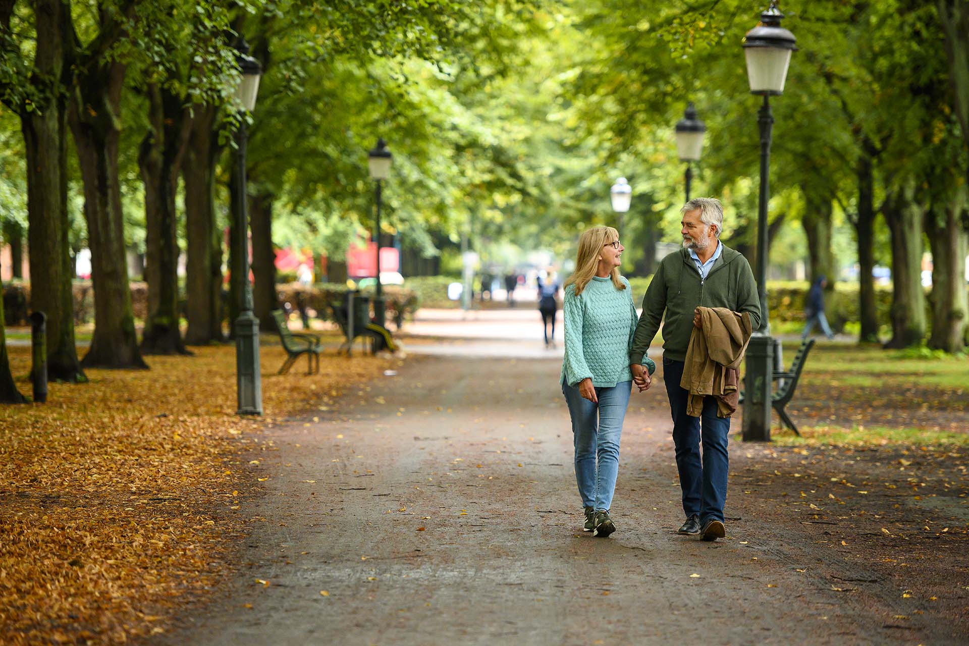 Ett par som går och håller handen på en gångväg i en park