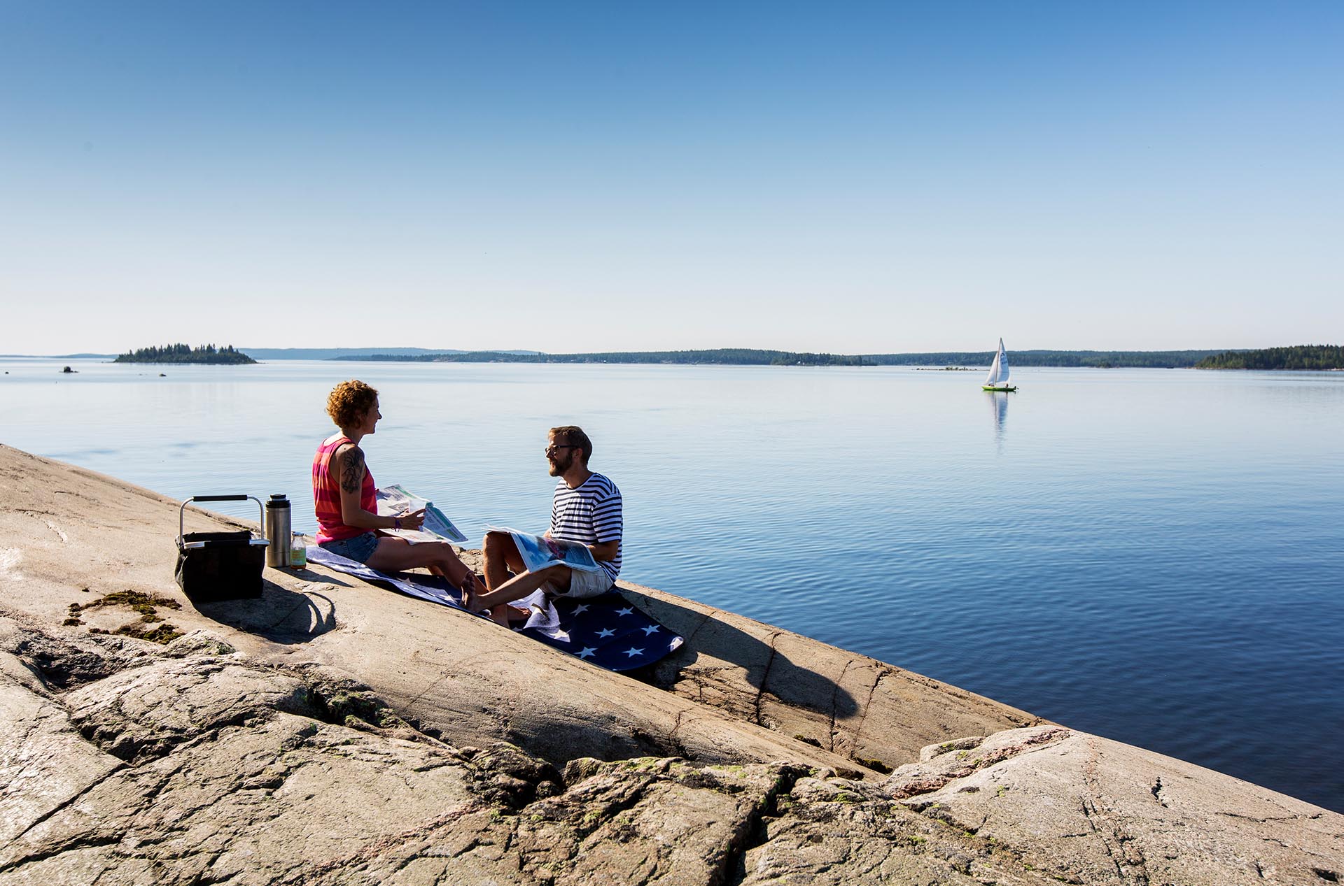 Ett par sitter på klipporna vid vattnet och fikar