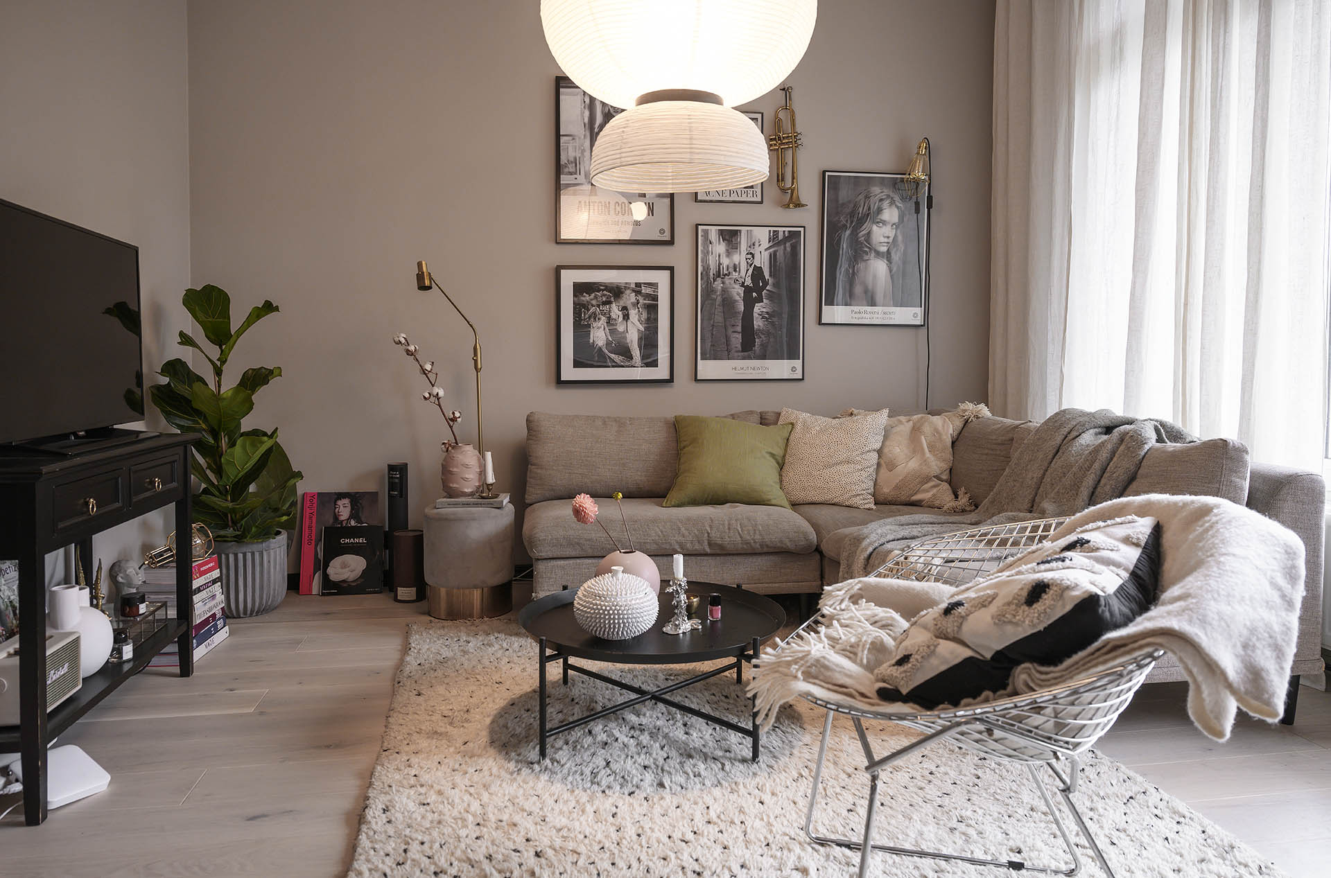 Ett beige vardagsrum med en stor beige soffa med en massa kuddar i. På golvet ligger en ljus luddig matta och ett svart soffbord på