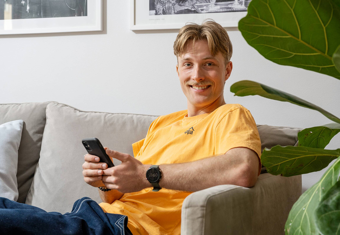 En kille i gul tröja gör en felanmälan via sin mobil till Heimstadens Mina Sidor.