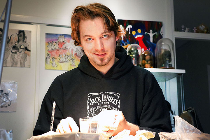En kille med brunt hår och en svart tröja som det står Jack Daniels på sitter vid sitt köksbord
