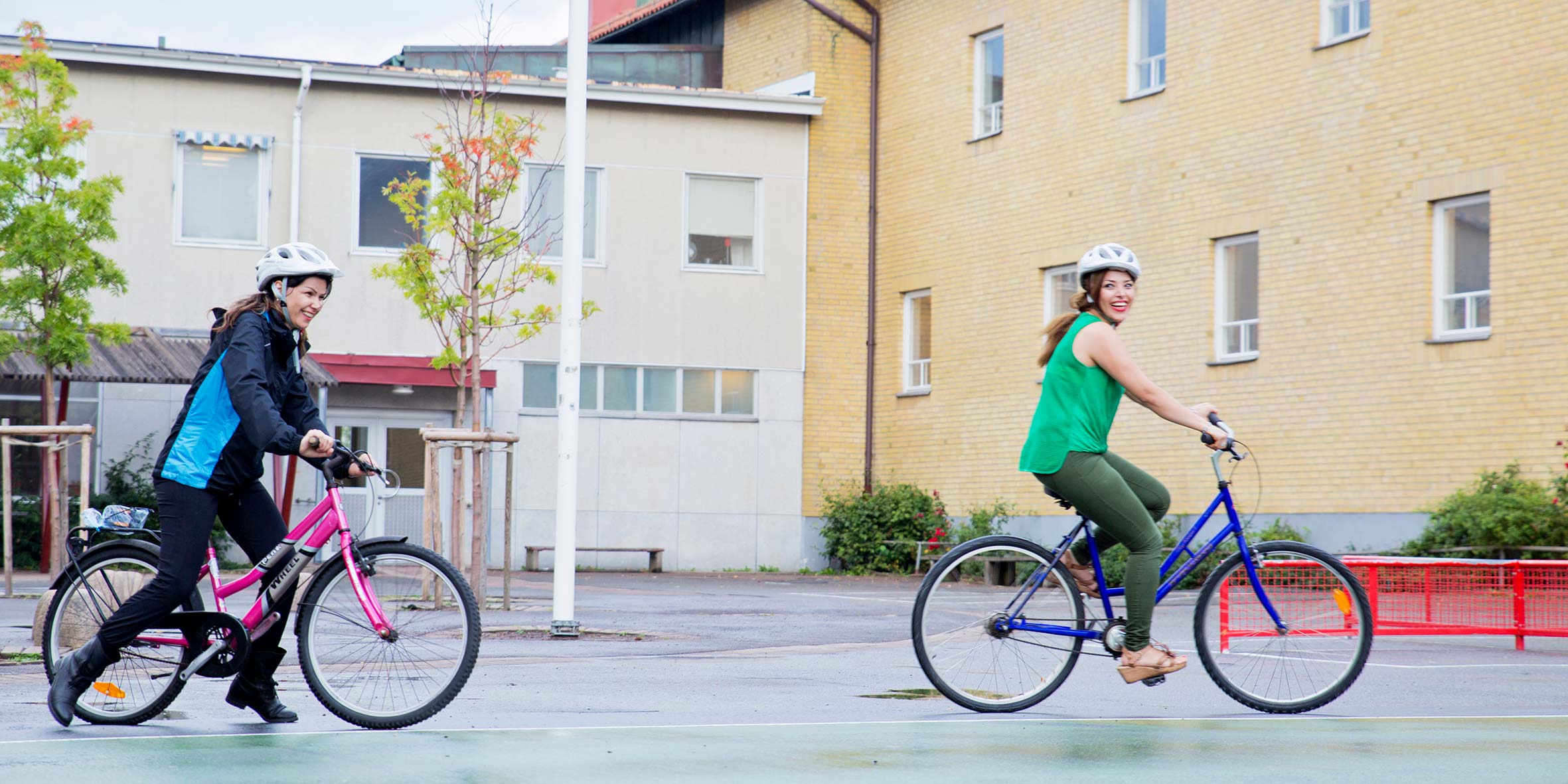 Två kvinnor som cyklar utanför en gul byggnad