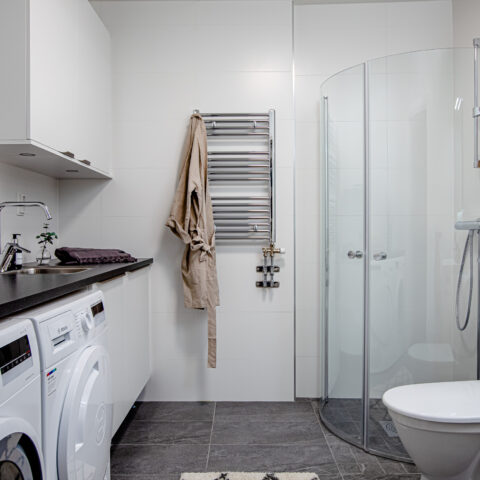 Badrum där man ser toalett, dusch, tvättmaskin och torktumlare.