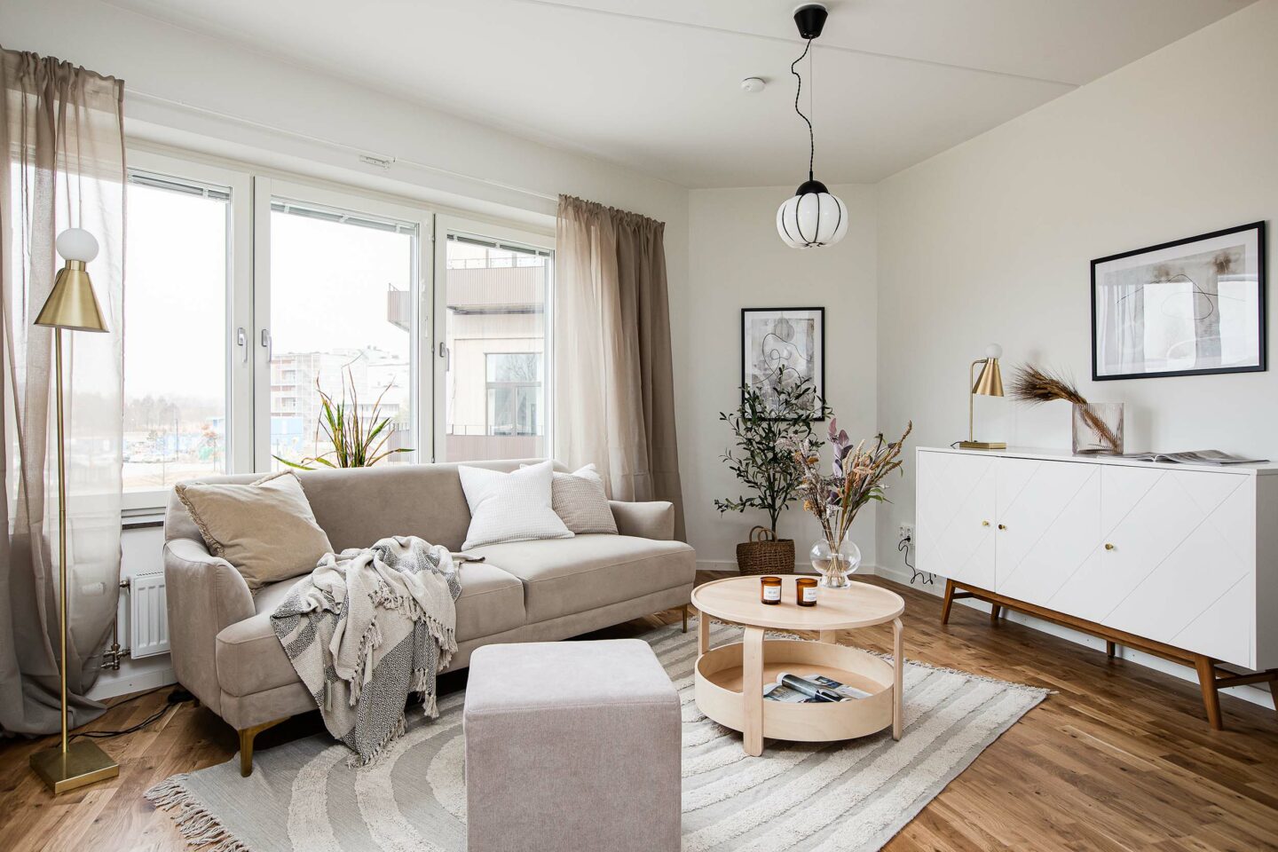 Ett vardagsrum med en stor beige soffa, ett soffbord i trä och ett vitt sideboard.