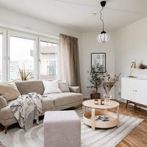 Ett vardagsrum med en stor beige soffa, ett soffbord i trä och ett vitt sideboard.
