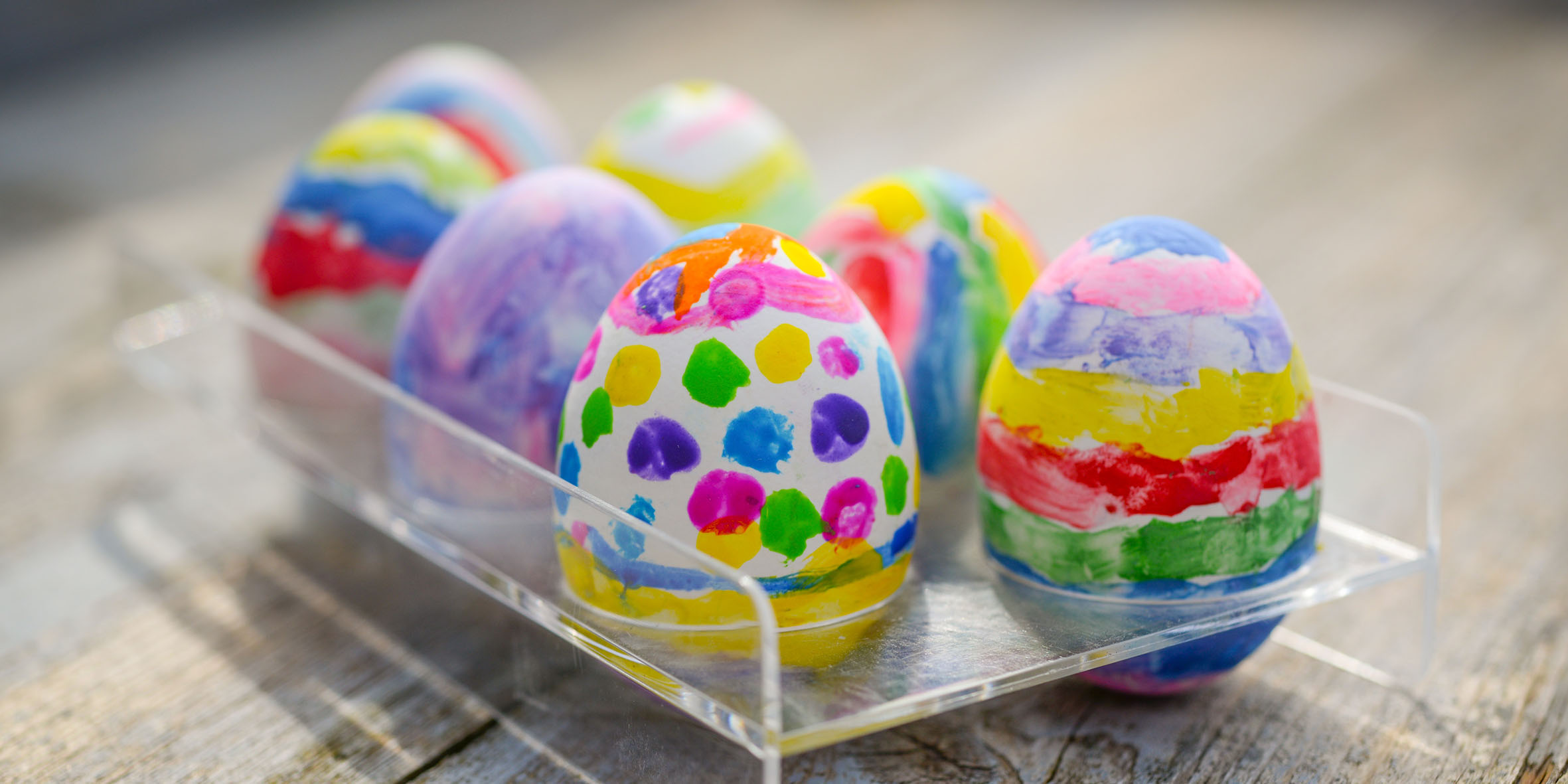 Ägg som är målade med alla möjliga färger och motiv som står i en plasthållare