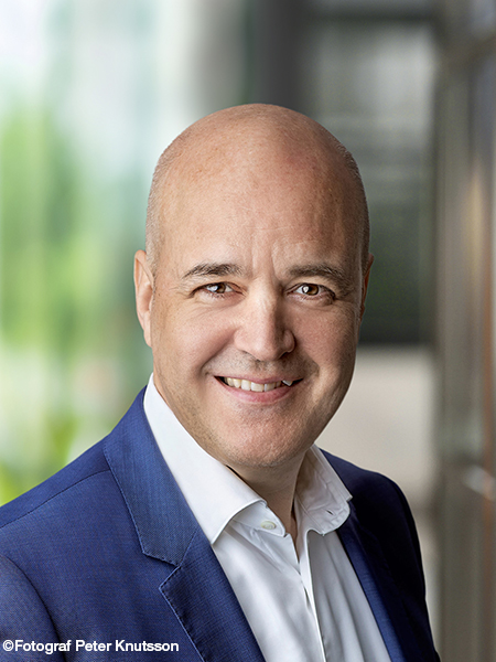 En skallig man i vit skjorta och havsblå kavaj ler mot kameran