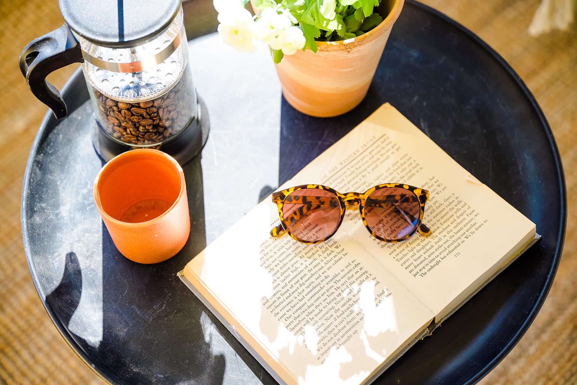 Ett svart bord som det ligger en bok, solglasögon och en orange kaffekopp på