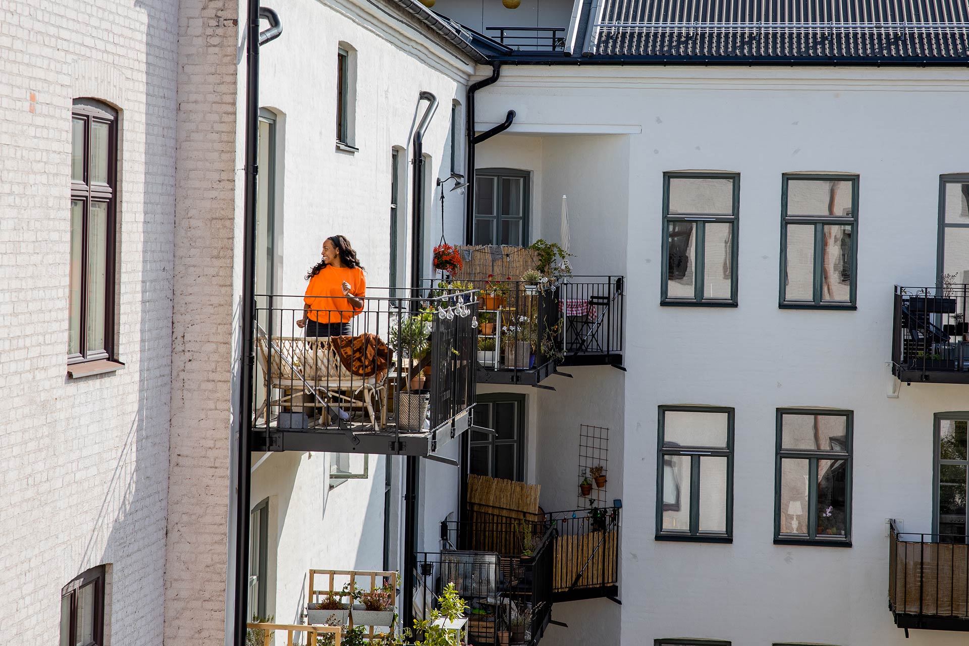 Ett vitt bostadshus där man ser en kvinna med orange kläder står på en balkong