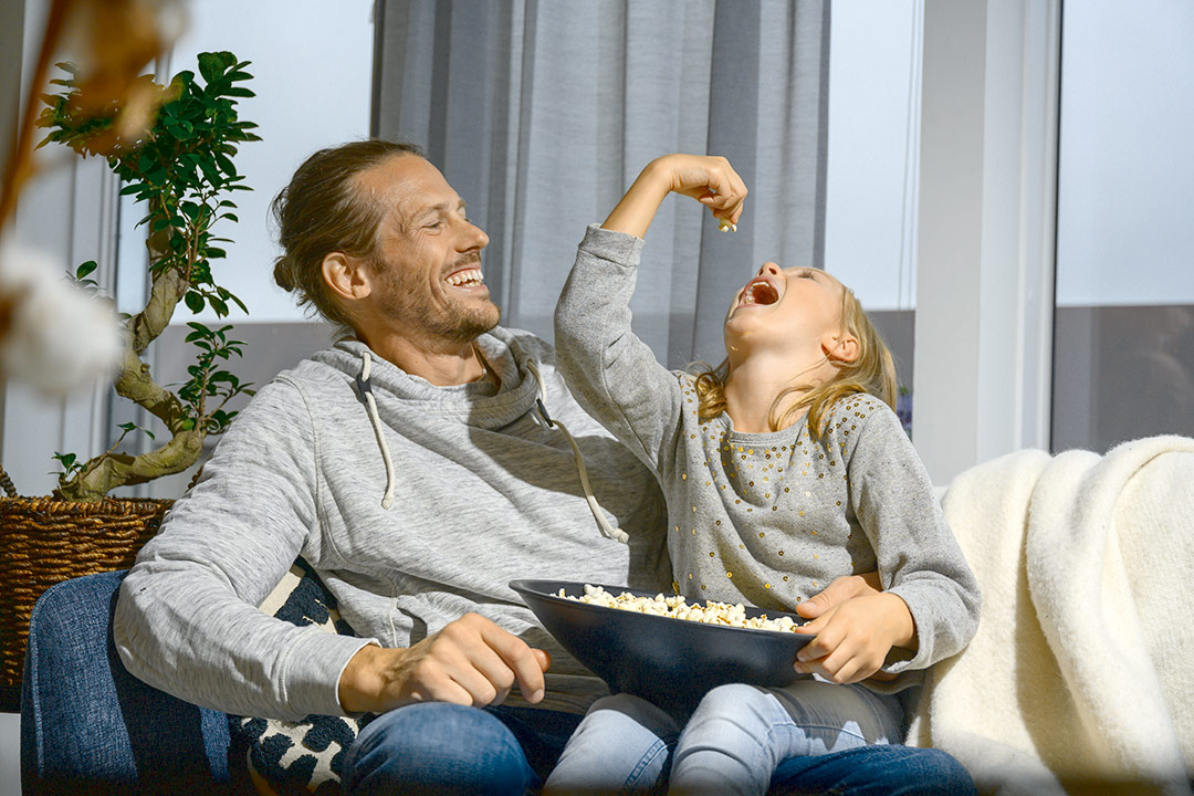 man och barn sitter i soffa, barn äter popcorn