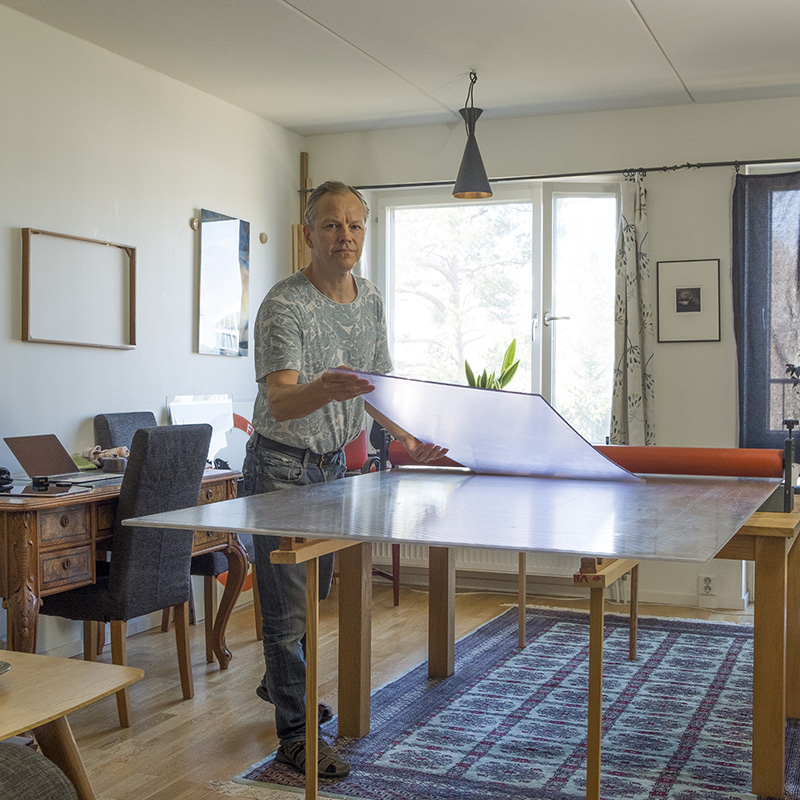 En man står i ett rum och håller på med några skivor på ett stort och högt bord