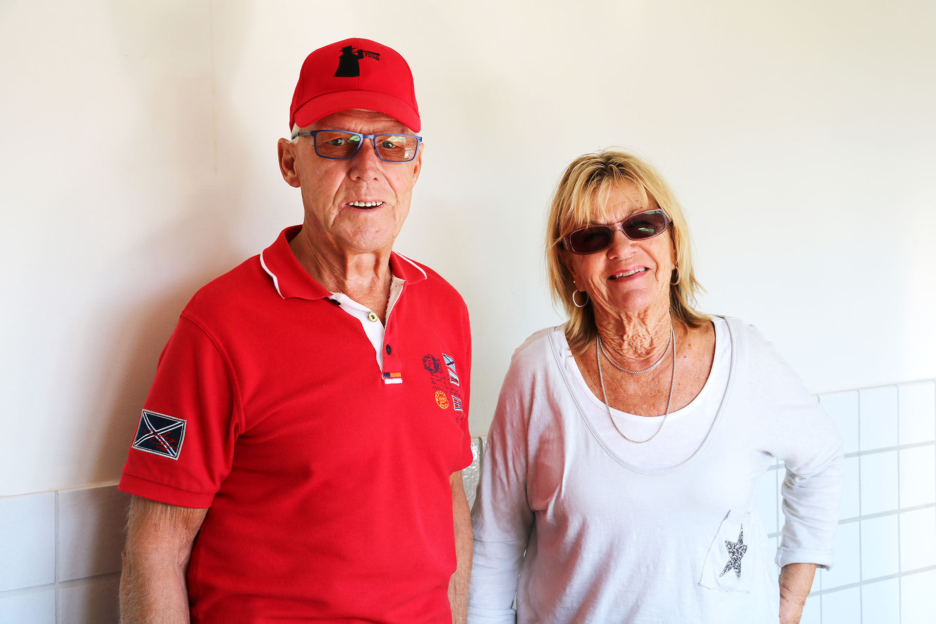 En äldre man med en röd tröja och en röd keps, står bredvid en kvinna med solglasögon och en vit tröja