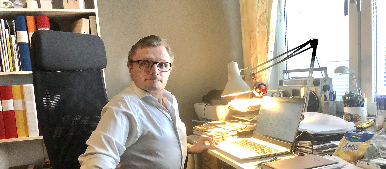 En man i vit skjorta sitter vid sitt skrivbord i hemmet