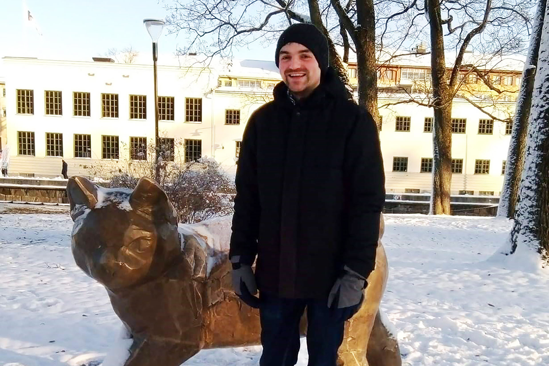 En man i jacka och mössa står vid en skulptur i snön