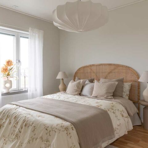 Ett ljust och vitt sovrum med en stor säng som har en rottinggavel bakom sig