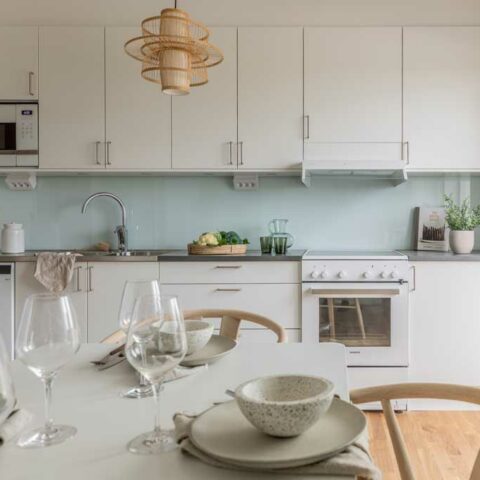 Ett kök med vita luckor och ett vitt köksbord med trästolar