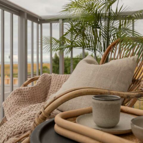 En balkong med en rottingmöbel som det är ljusa textilier i