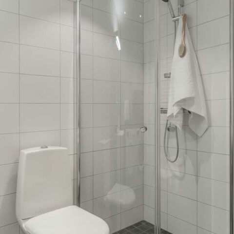 Ett vitt badrum i kakel och en vit toalett