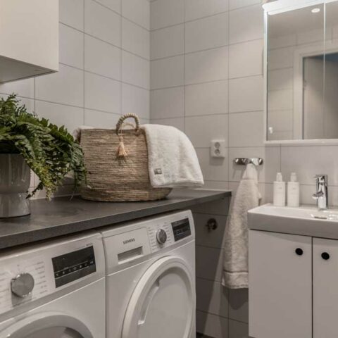 Ett ljust och vitt badrum där man ser en torktumlare och en tvättmaskin