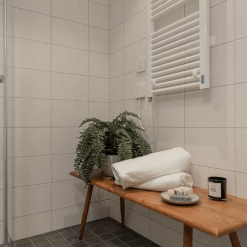 Ett vitt kaklat badrum med en avlång sittmöbel som det ligger ihoprullade handdukar på