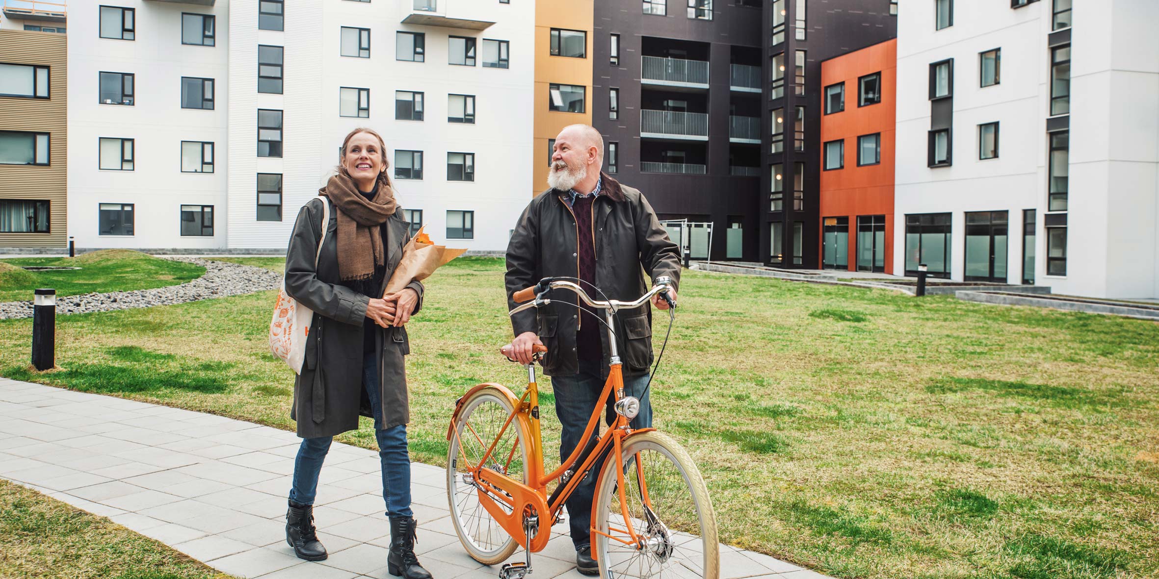 En kvinna har en blombukett i famnen och man som leder en cykel i ett bostadsområde