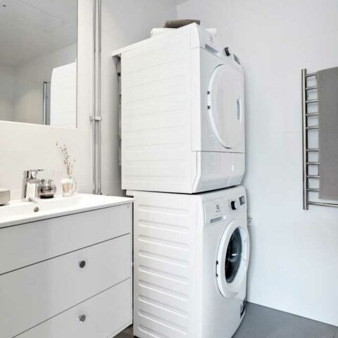 Ett badrum där man ser ett stort vitt tvättställ och en kombinerad tvätt- och torktumlare