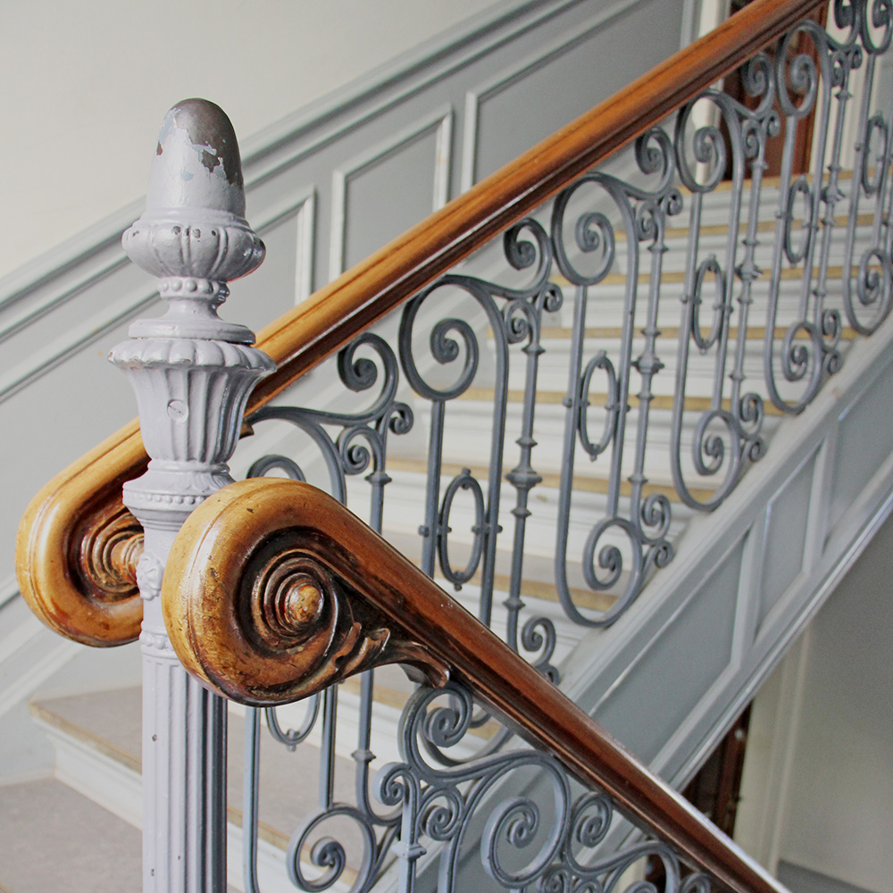 Ett trapphus och en närbild på räcket som är i trä och grått smide