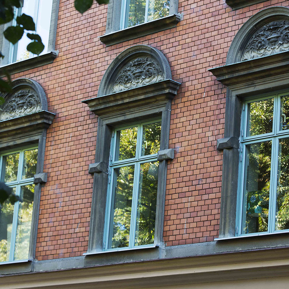 en närbild på en rödbrun tegelfasad och fönstren som är koppargröna