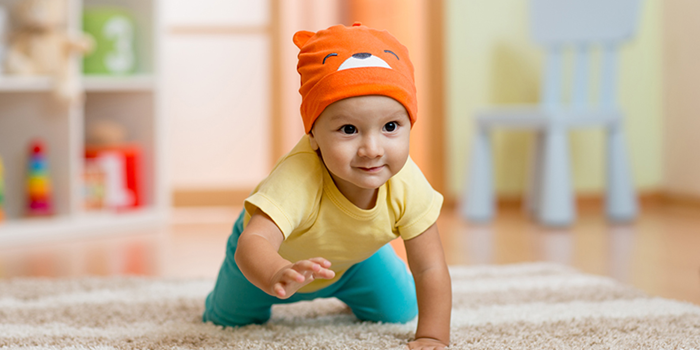 En liten bebis i orange mössa och gul tröja kryper runt på golvet
