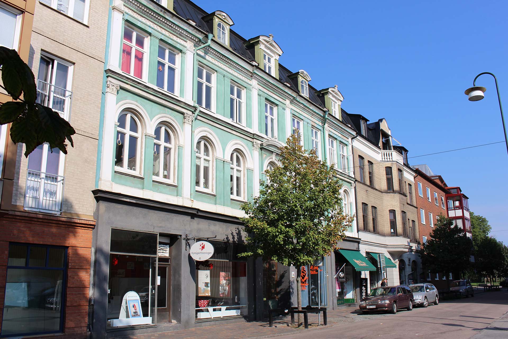 En mintgrön sekelskiftesbyggnad med butikslokaler i botten