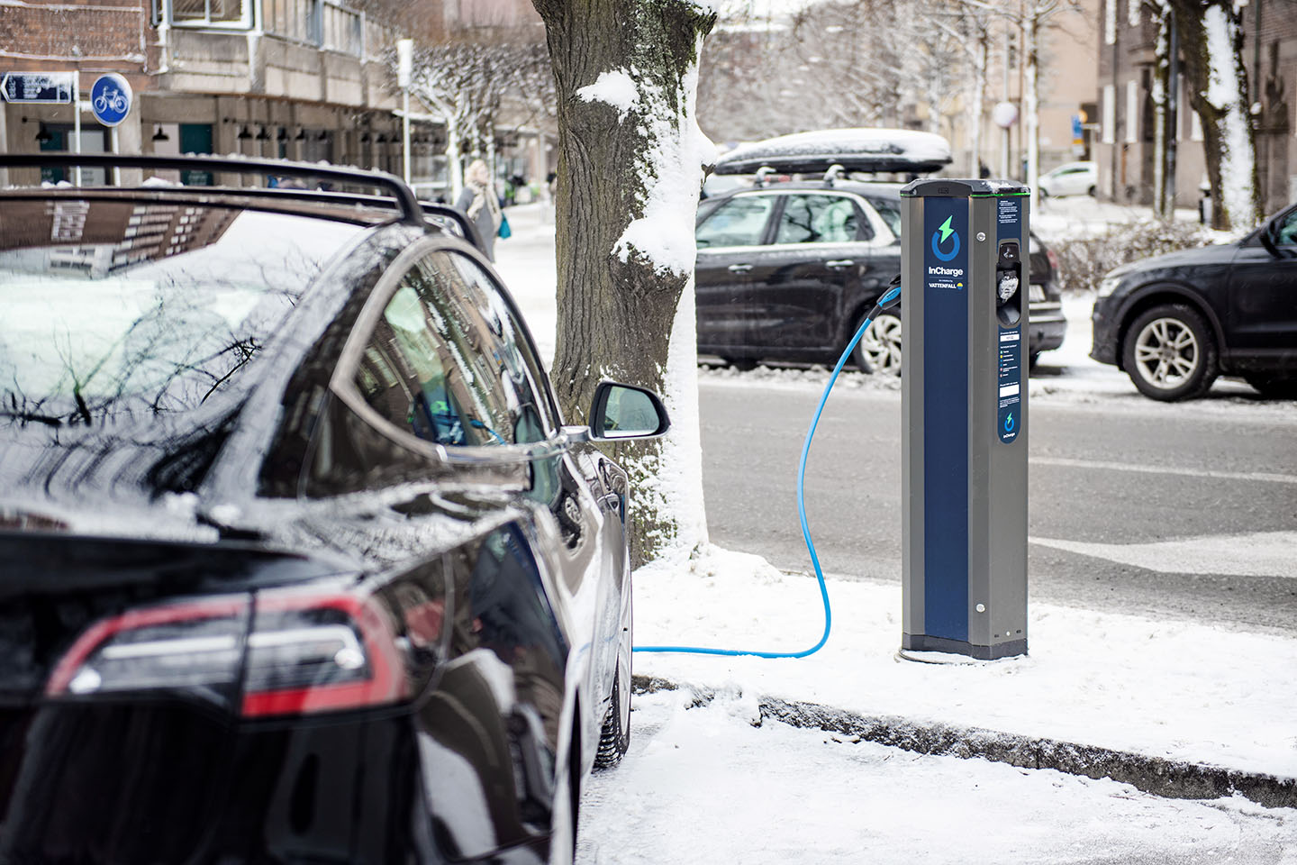 En svart bil laddas i en laddstolpe ute på en snöfylld gata.