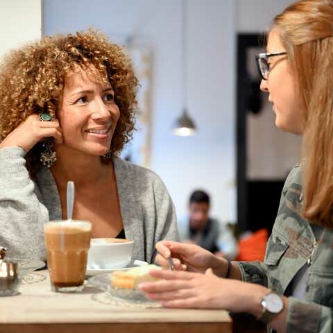 Två tjejer sitter på ett café och dricker kaffe och äter en bakelse